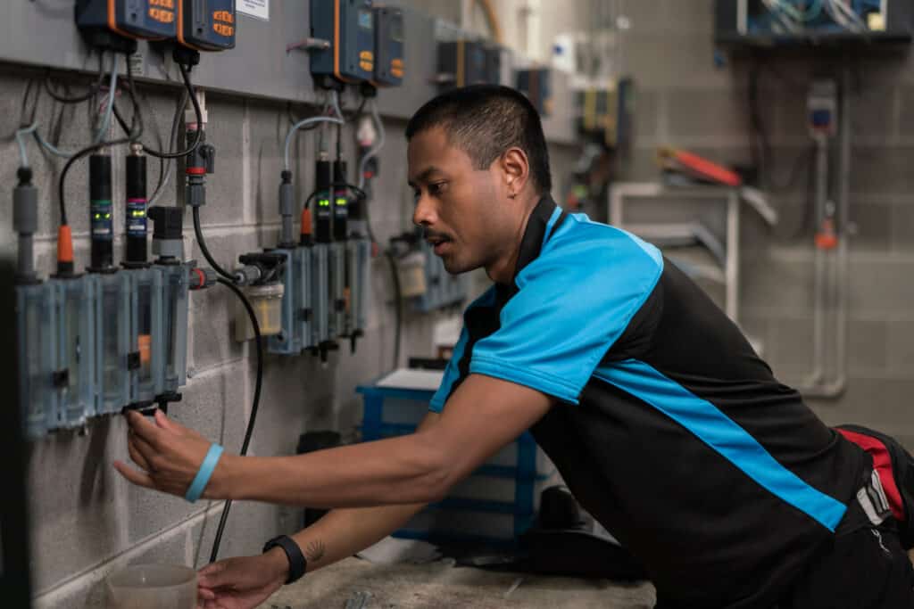 A man works in the plant room at a public pool. He tests the water quality.